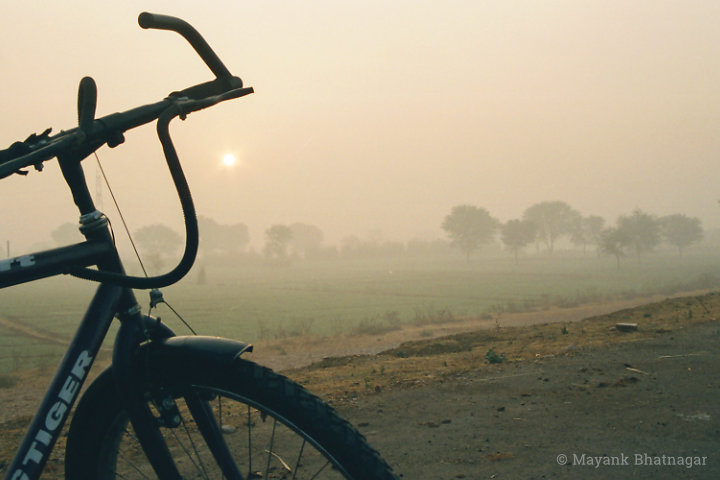 A bicycle in the foreground framing the sun rising behind above misty green fields