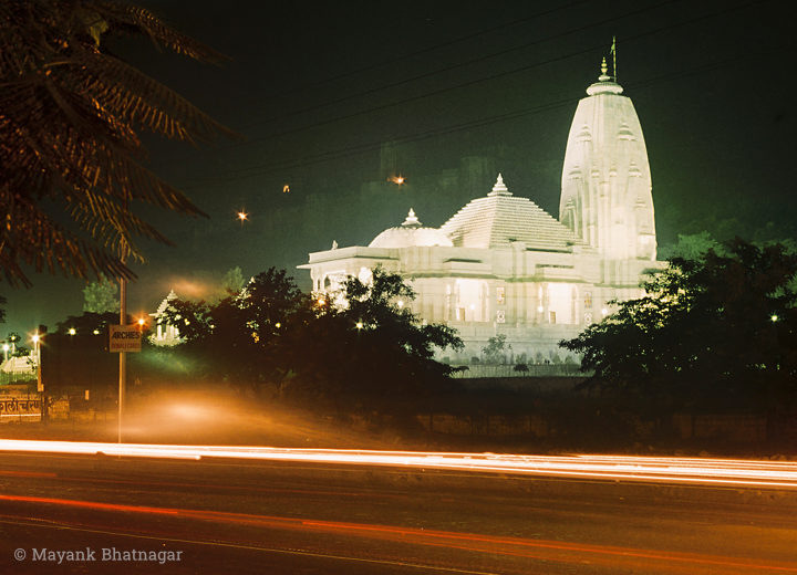 Light streaks of passing vehicles in the foreground with a brilliantly lit-up white marble temple behind