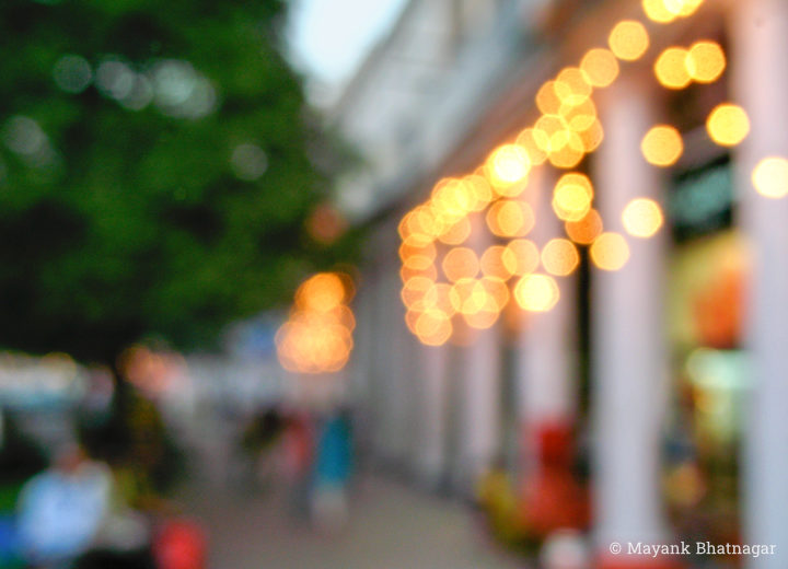 Blurred photograph of the exterior of a CP block, revealing pillared corridors, lighting decorations, people and a tree