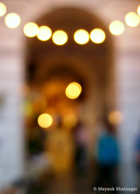 Light bulb decorations over a corridor arch, with people and shops behind