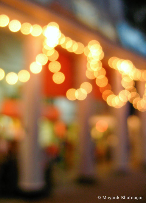 Night shot of lit up decorative bulbs hanging over round pillars, with shop windows behind