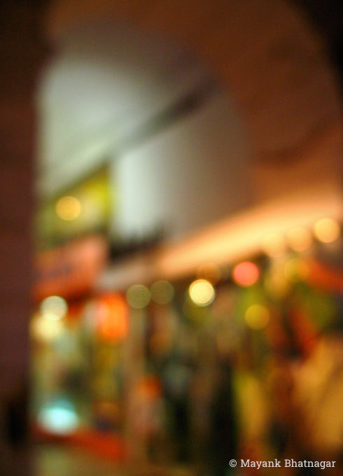 Blurred / unfocussed photograph of colourful, lit up shop windows below an archway