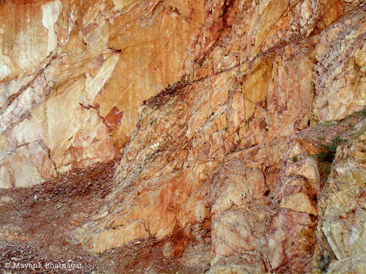Heavily textured and scarred rock face in shades of orange colour