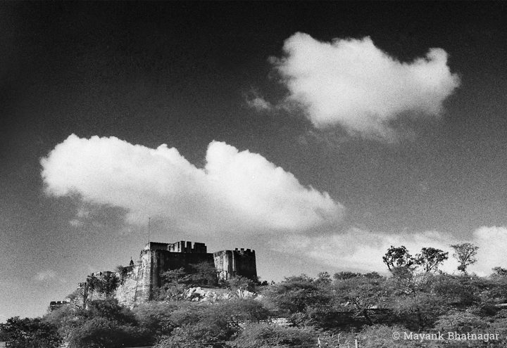 Two large clouds floating in the sky, above a fortress on a hilltop