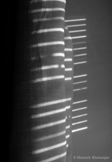 Horizontal streaks of sunlight falling at different levels on a folded curtain
