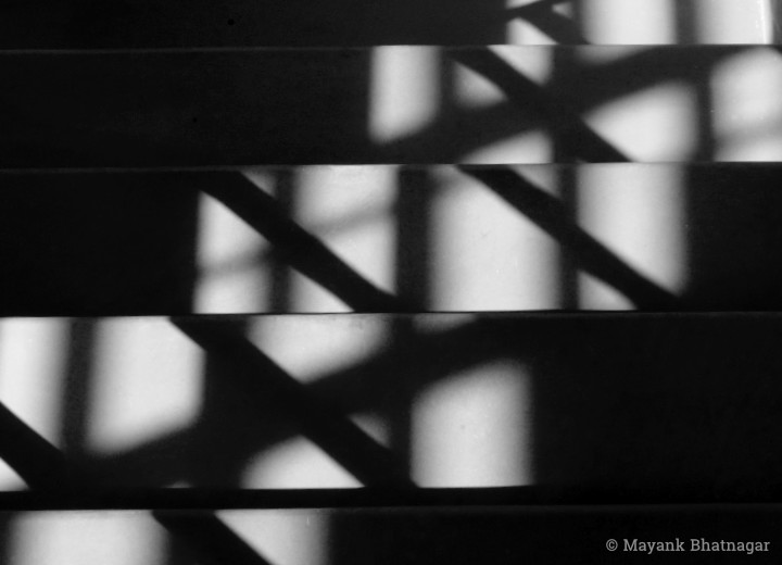Top view of light from a grilled window falling diagonally on stairs and creating an abstract, zig-zag pattern
