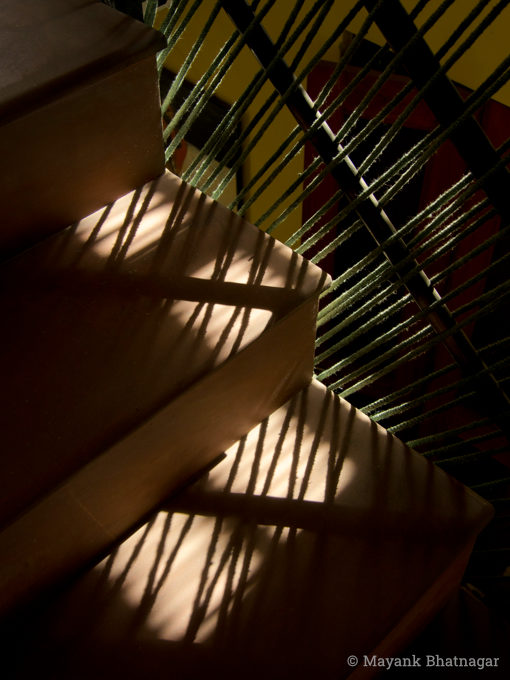 Patches of light from a window falling on ropes tied to a railing and on adjacent stairs