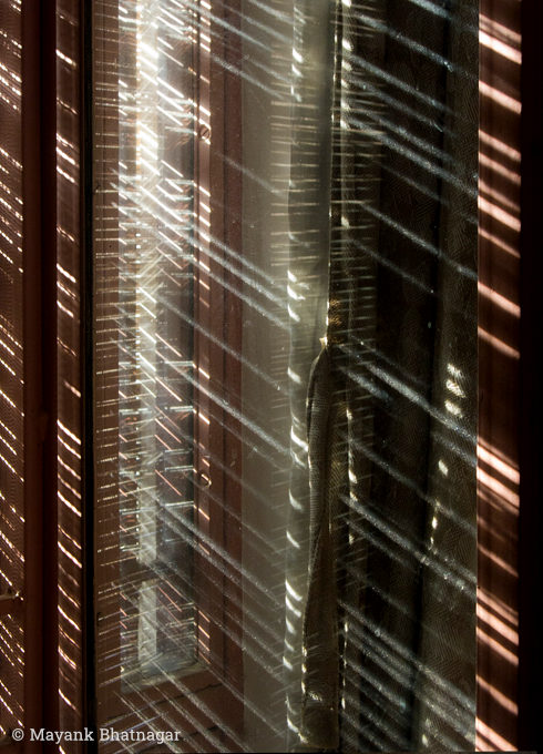 Thin, diagonal sreaks of light falling on window panes, window glass and on adjacent curtains