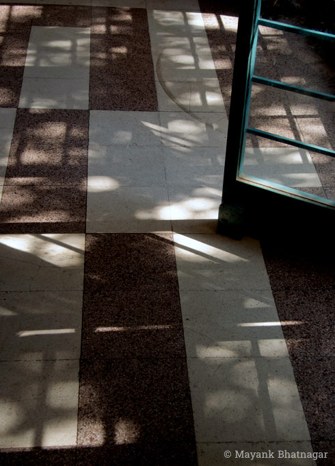 Light patterns from a large grilled window falling on textured floor tiles