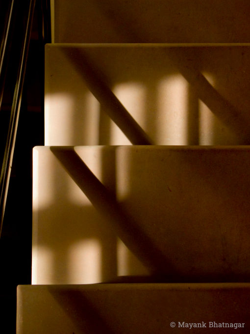 Tight shot of light and shadows from a grilled window and a railing falling on the stairs below
