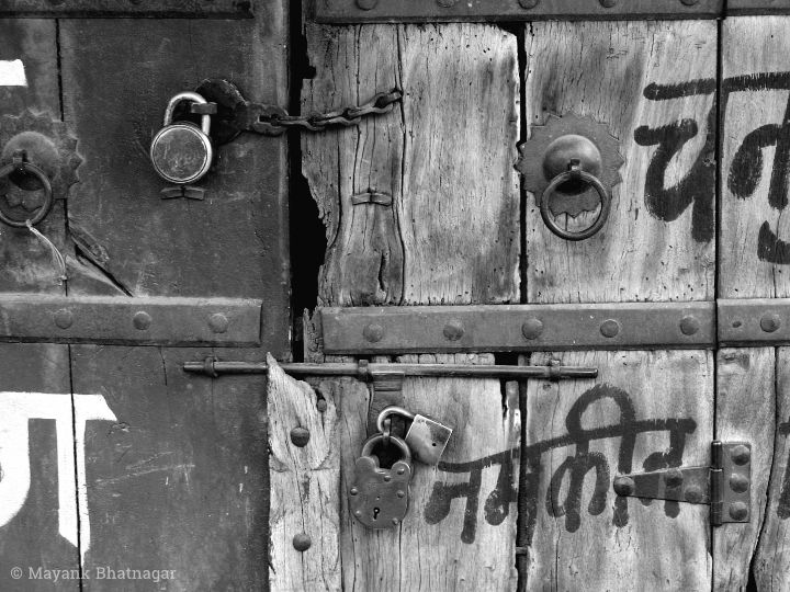 A textured wooden door with metal handles, a chain, locks and words painted in hindi
