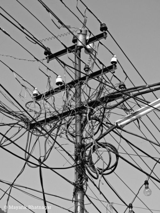 An electricity pole loaded with wires, a tube-light and some bulbs