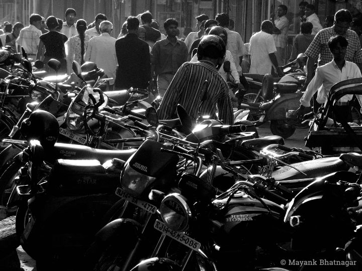 High contrast photograph chock-a-block with parked motorbikes (in the foreground) and people