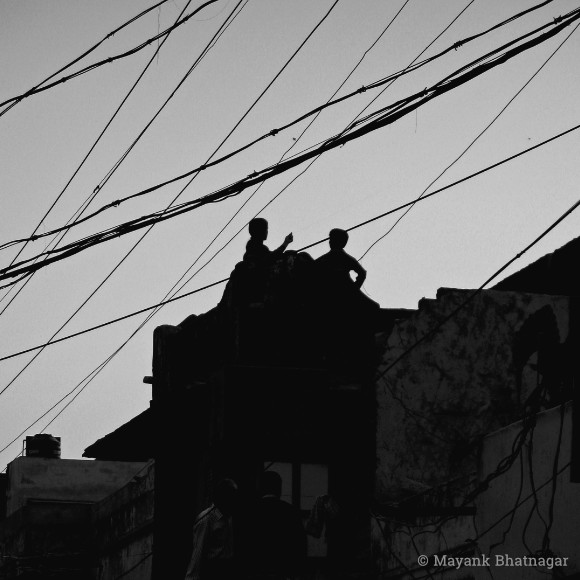 Silhouette of two children on the roof of a building, with electricity wires criss-crossing above