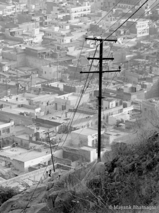 Fill-frame shot from a hill, of lots of houses below, and two poles connected by wires leading to them