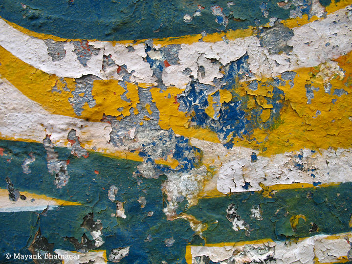 Horizontal, curved layers of bluish-green, white and deep yellow paint, peeling all over