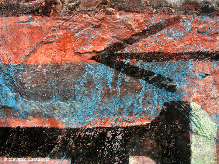 A black arrow over red, blue and black bands of paint, on a heavily textured stone wall