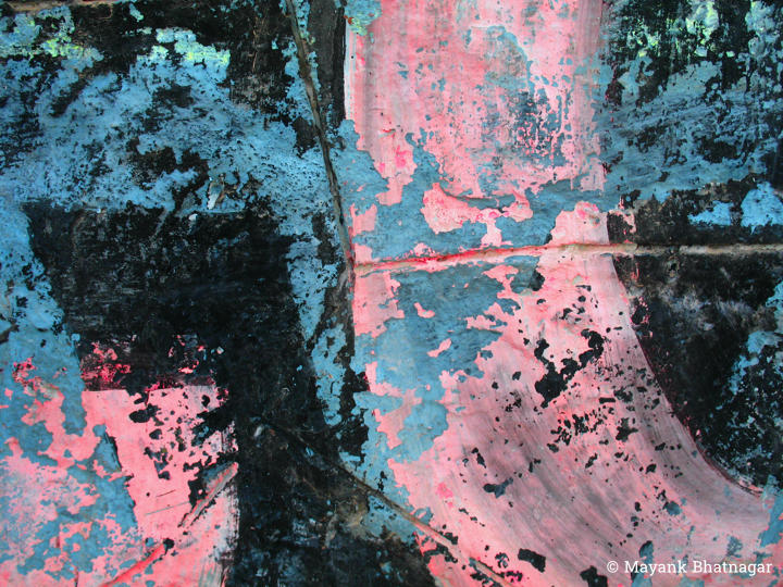 Closeup of painted English letters with black, light blue and pink paint peeling off the surface