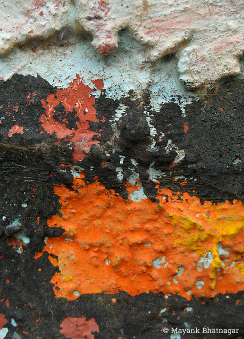 Closeup of deep orange, black and sky blue rough paint marks on a thickly textured surface