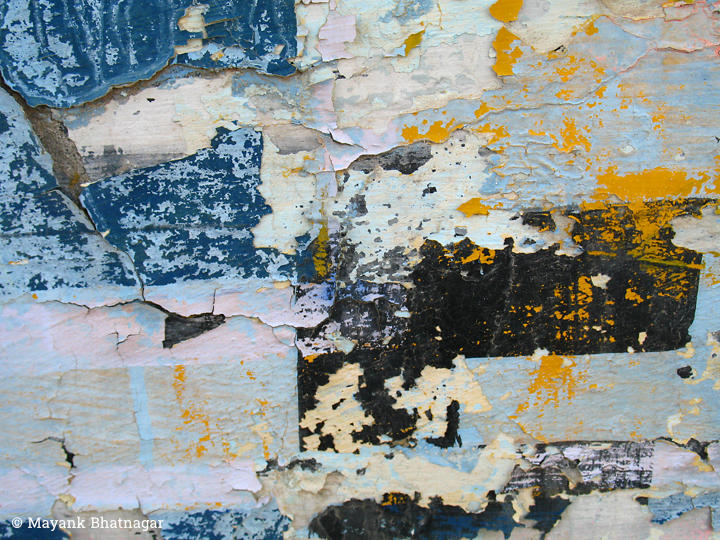 Blue, white, yellow and black paint peeling off the textured surface of a wall