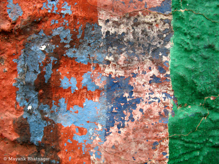 Vertical layers of peeling red, white and dark green paint revealing blue paint below