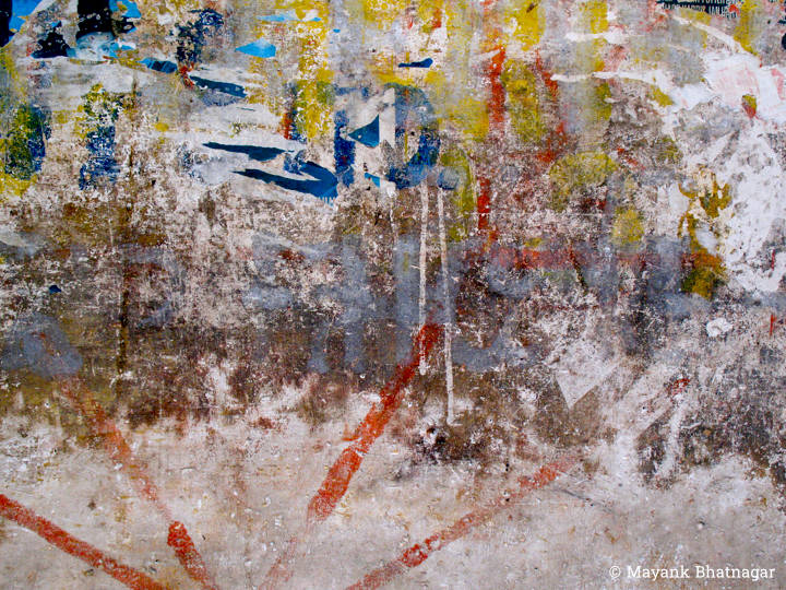 Worn out, heavily textured, colourful paint marks and remnants of paper on an old wall
