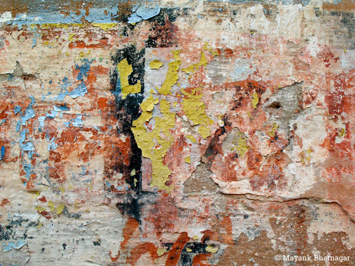 Multi coloured paint peeling off an old textured wall, giving an overall abstract look and feel