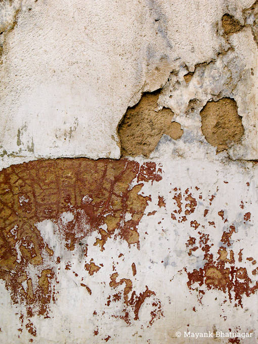 Plaster peeling off an old white painted wall, revealing textured maroon and brown layers below