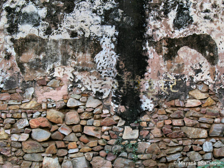 Heavily textured wall with layers of paint above and exposed multi colour stones below