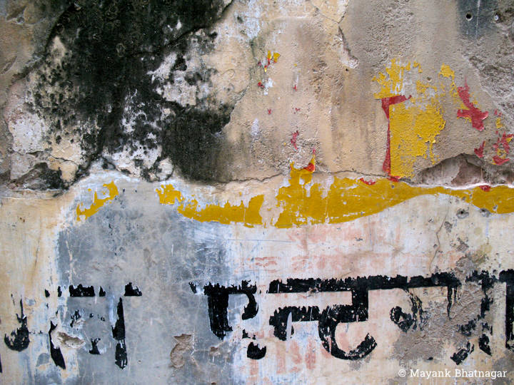 Worn out paint and some broken plaster on an old wall with remnants of hindi lettering towards the bottom