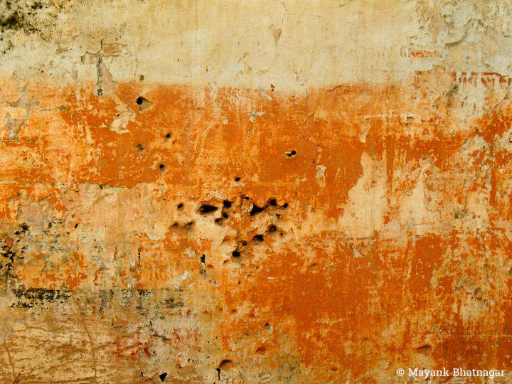 A textured, yellowish wall with worn out red paint and some holes in the middle