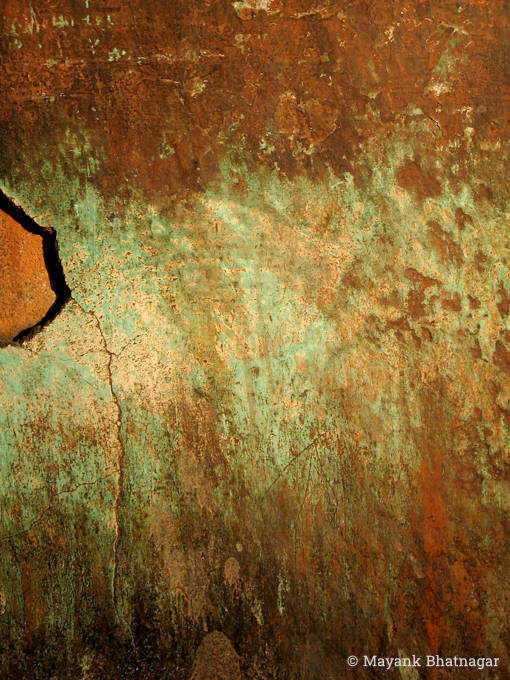 Closeup of a heavily textured wall with deep red stains over light green colour, and plaster broken on one side
