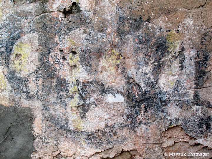Remnants of paint, in pastel shades and black, on an old, finely textured, partly cemented stone wall