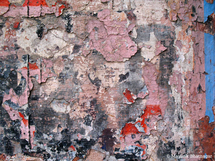 Many layers of torn paper and paint peeling off an old wall, in dominant pink colour