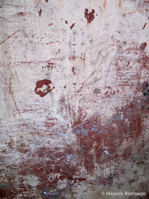 Maroon paint and scratches on a textured white wall, darker towards the bottom