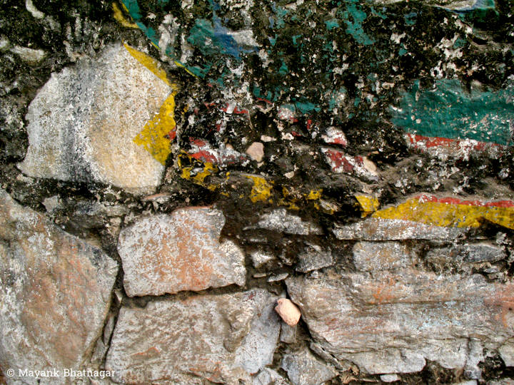 Worn out paint above large exposed stones on an old, heavily textured wall