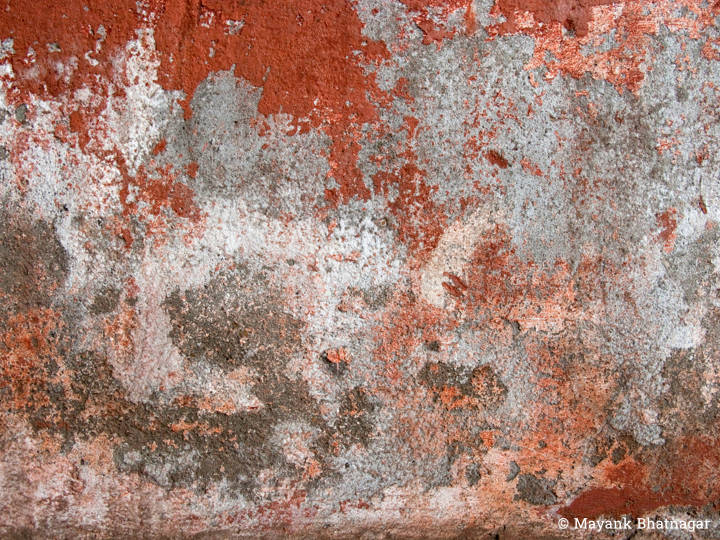 Many layers of worn out red, grey and white paint on heavily textured surface of a wall