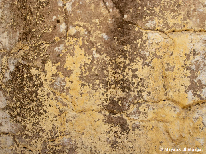Textured, worn out brown paint over an old, pale yellow wall