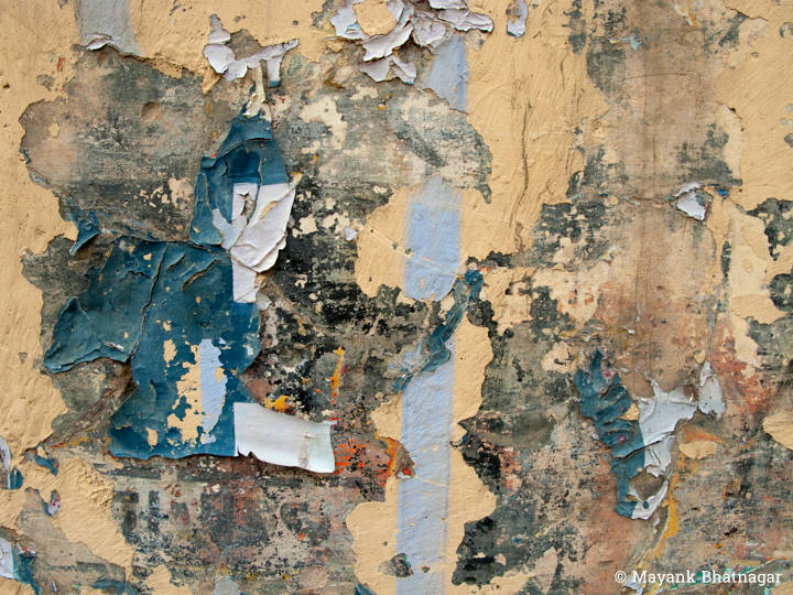 Torn posters and peeling paint revealing underlying texture, on the surface of a beige coloured wall