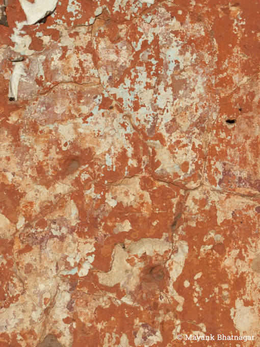 Dark orange or 'Geru' colour peeling off an old wall with some large, shallow cracks on it