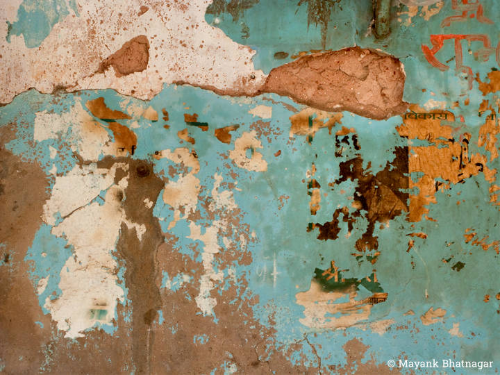 An old, turquoise painted wall with plaster and paint peeling off at places, along with remnants of a torn poster