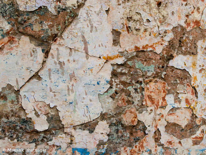 White plaster with paint marks on it peeling off an old wall, revealing a textured brown layer underneath