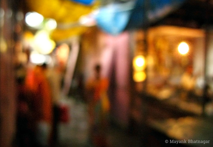 Shoppers in a narrow lane lit with bulbs, with stalls on both sides