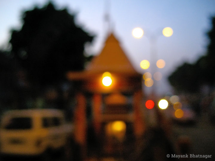 A small temple with street lights, traffic and tree silhouettes around it