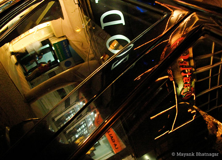 Reflections of a market corridor and neon signs on window glasses and black body of a car