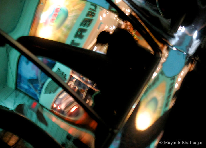 Blurred reflections of a colourful shop exterior and a human figure on the glass and body of a car