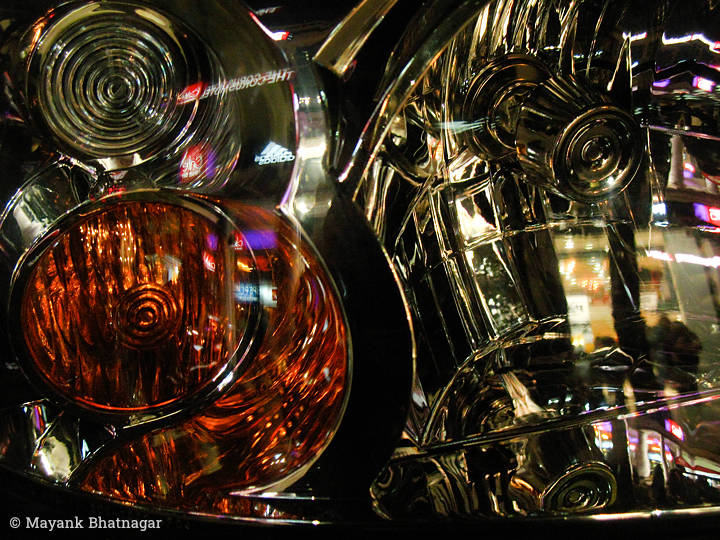 Reflections of shop lights and signs on the outlines of shiny, geometric headlights of a car