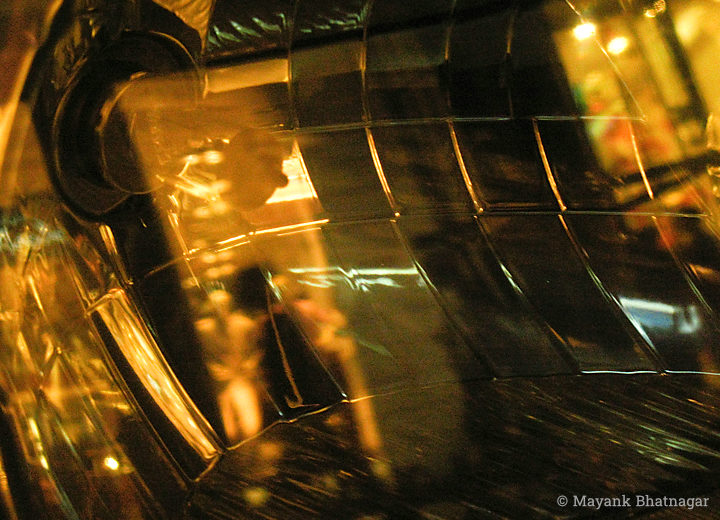 Reflections of a passerby and shops behind on a mirror-like car headlight with geometric patterns