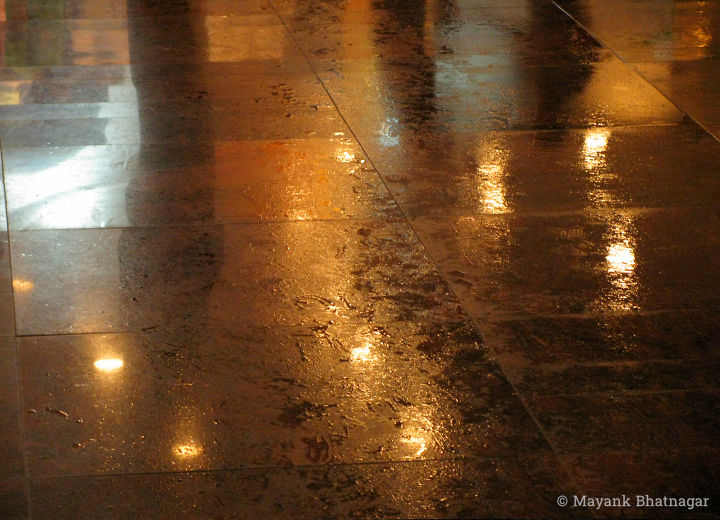 Reflections of ceiling lights and shadows of people on wet floor tiles, at night