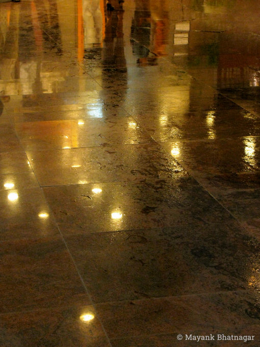 Reflections of ceiling lights and people on wet floor tiles, at night